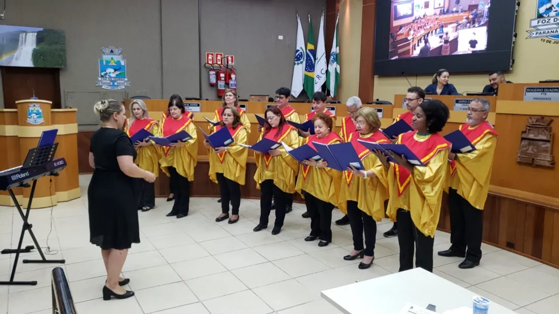 Coral Cisne Branco de túnicas douradas cantando em sessão na Câmara de Vereadores de Foz do Iguaçu